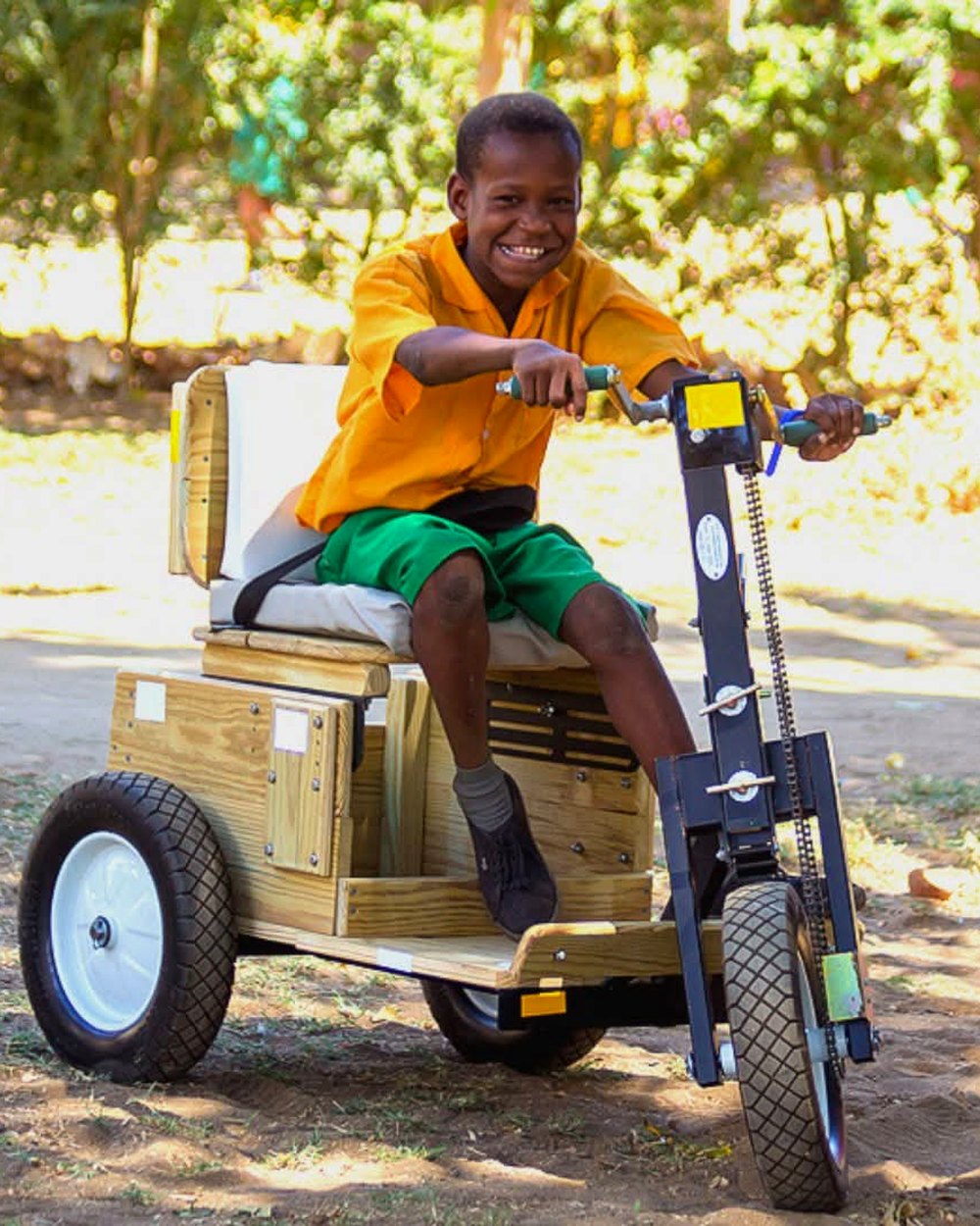 A boy with a disability smiling as he rides a hand-powered tricycle provided through donor support